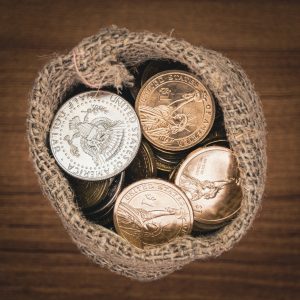 Dollar coins in burlap bag on wooden table