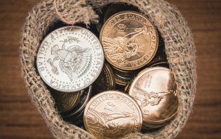 Dollar coins in burlap bag on wooden table